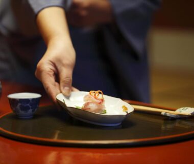 Hand placing small ceramic dish on lacquer tray with chopsticks and tea at Kinjohro, Chubu, Ishikawa