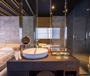 Sink on wooden vanity, glass shower and low bed in Kinnotake Saryo room, Kanagawa