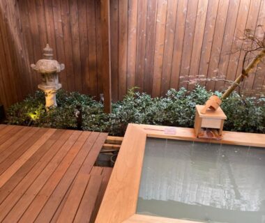 Wooden onsen bath with decking, stone lantern and garden shrubs at Kinnotake Saryo Kanagawa