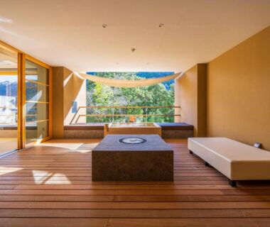 Spacious wooden lounge with low stone table, bench seating and large window overlooking trees at Kinnotake Tonosawa, Kanagawa