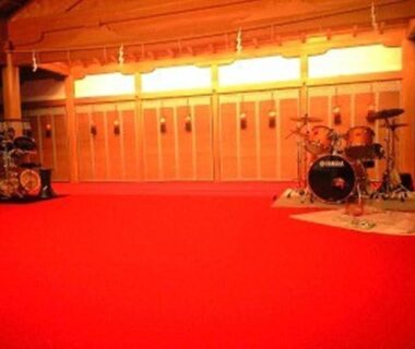 Drum kits on red carpeted stage with wooden backdrop in a ryokan event hall at Kinokuniya Jinpachi Nara