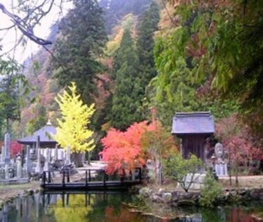 Pond with stone statues and shrine at Kinokuniya Jinpachi surrounded by autumn trees in Nara