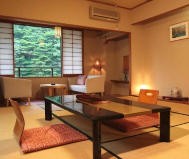 Tatami room with low black table, floor cushions, shoji screens, seating area and window overlooking greenery at Kinokuniya Ryokan Kanagawa