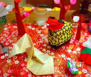 Origami cranes and fabric dolls on red patterned cloth centerpiece inside Kinokuniya Ryokan, Kanagawa