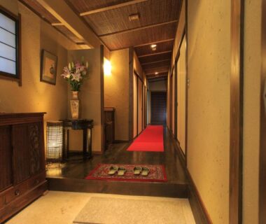 Shoji window corridor with wooden chest, floral arrangement, slippers and red runner at Kinokuniya Ryokan Kanagawa