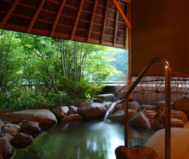 Sheltered rock-lined onsen bath opening to lush garden at Kinosaki Onsen Nishimuraya in Hyōgo, Kansai