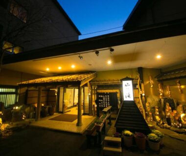 Lit wooden entrance with covered walkway and lanterns at Kinosato Yamanoyu in Oita