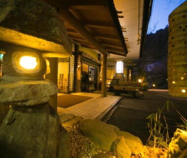 Traditional ryokan entrance with stone lanterns, wooden architecture and warm evening lighting at Kinosato Yamanoyu in Oita, Kyushu