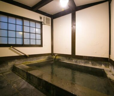 Stone-lined indoor soaking tub with shoji window and wooden beams at Kinosato Yamanoyu Ōita