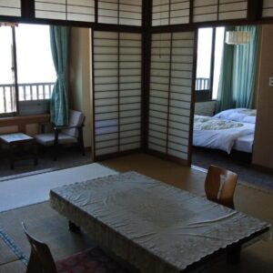 Tatami room with low table, low-back floor chairs, shoji screens and adjoining Western beds at Kinpokan in Mie