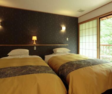 Twin bed room with shoji sliding doors opening to balcony and green foliage at Kinseikan Seseragi Gunma