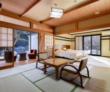 Spacious tatami room with low table, shoji screens, bed and balcony at Kinshuusanso in Gunma
