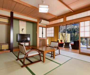Traditional tatami room with low wooden chairs, shoji screens and sliding doors opening to a small garden at Kinshuusanso, Gunma