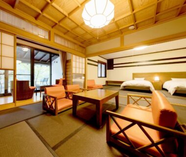 Tatami room with low table, lounge chairs, twin beds and shoji screens at Kinshuusanso in Gunma