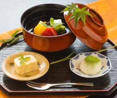 Lacquer tray with lidded bowl of fruit, rolled omelette and a small sweet on orange cloth