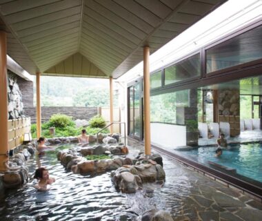 Indoor rock-lined onsen baths with glass wall overlooking greenery at Kinugawa Hotel Mikazuki, Tochigi