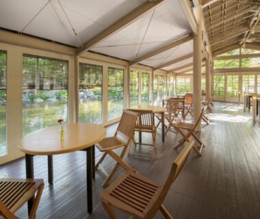Wooden chairs and tables facing a calm pond through large windows at Kinugawa Park Hotels, Tochigi, Japan
