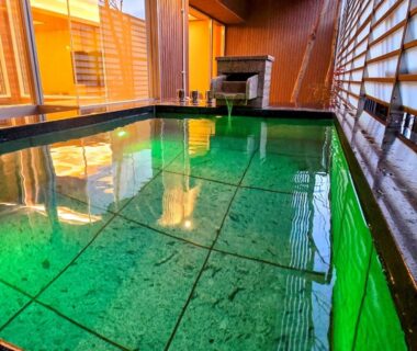 Tiled indoor onsen bath with green water, wooden paneling and shoji screens at Kinugawa Plaza Hotel, Tochigi