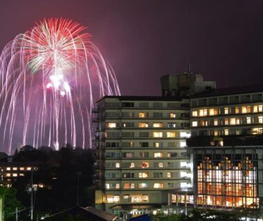 Nighttime fireworks display above illuminated Kinugawa Plaza Hotel building in Tochigi prefecture