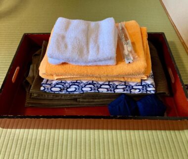 Folded towels and linens with small amenities on a wooden tray atop tatami mat in Kirishimaya Ryokan, Gunma