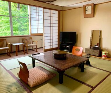 Traditional tatami room with low lacquered table, zabuton cushions, shoji screens and window seating overlooking green trees