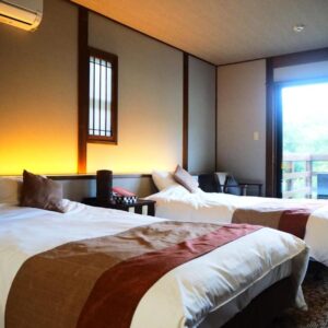 Twin beds, bedside lamps and seating area by a sliding glass door to balcony at Kisara in Mie