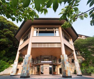 Front entrance of Kissho Caren with stone pillars, wooden balcony and surrounding greenery in Shizuoka