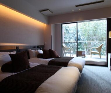 Contemporary twin beds with throws, glass doors opening to balcony chairs and leafy greenery at Kitanokaze Saryo, Kanagawa