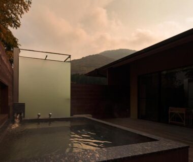 Stone-lined onsen bath on wooden deck at Kitanokaze Saryo in Kanagawa with mountain backdrop at dusk
