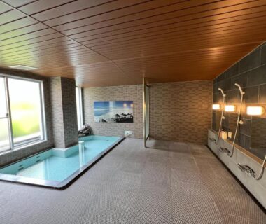 Tiled indoor soaking pool with shower stations and large window at Kitashiga Holiday Inn Nagano