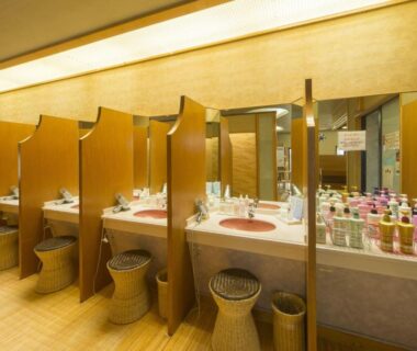 Communal vanity and dressing area with wooden booths, stools and assorted toiletries at Kohan-no-Yado Morimoto in Ishikawa