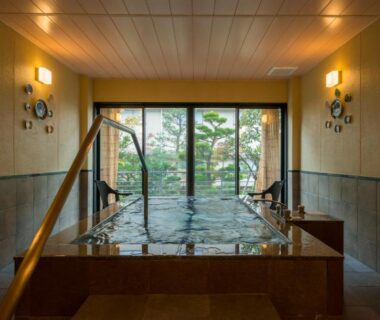 Stone-lined indoor onsen tub with handrail and garden view at Kohan-no-Yado Morimoto Ishikawa
