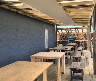 Covered wooden terrace with tables, benches and stacked firewood at Koinami in Mie