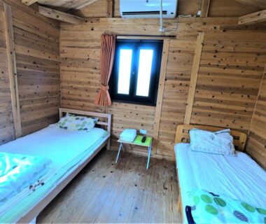Twin beds in wooden room at Koinami in Mie, Kansai with small window, bedside table and air conditioner