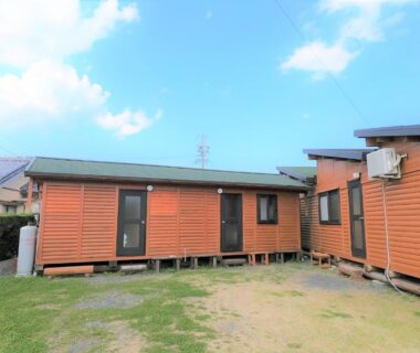 Exterior of small wooden cabins on raised foundations with grassy courtyard at Koinami in Mie, Kansai