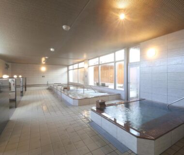 Spacious tiled indoor onsen with multiple pools, wooden accents and large windows at Kojohama Onsen Hotel, Hokkaidō