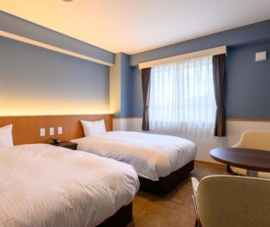 Two single beds with bedside lighting in a room at Kojohama Onsen Hotel, small table and chairs, Hokkaido