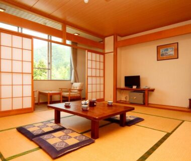 Tatami room with low table, shoji screens, floor cushions and a window with greenery at Komao Nagano