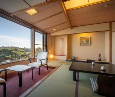 Traditional tatami room with low table and chairs facing large window overlooking bay and hillside in Miyagi