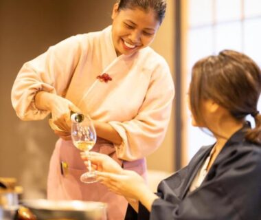 Staff in kimono pouring a drink for a guest during indoor ryokan dinner at Komatsuya Hachinobou, Shizuoka