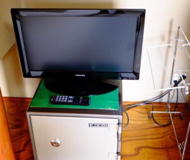 Flat-screen television on mini fridge in Komaya Ryokan room, Yamanashi, with metal clothes rack and remote