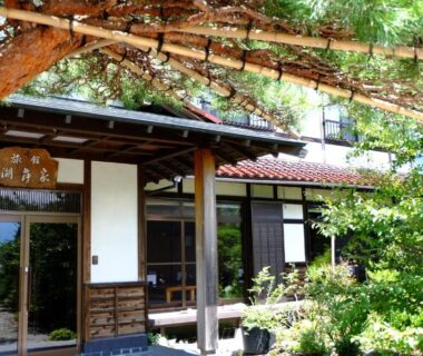 Wooden entrance with tiled roof and garden greenery at Komaya Ryokan in Yamanashi