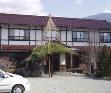 Exterior facade and entrance of Komaya Ryokan with yukitsuri canopy, gravel parking and mountain backdrop in Yamanashi, Chūbu