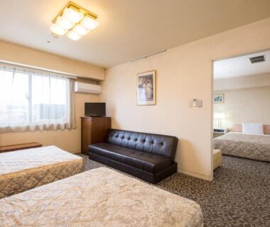 Spacious twin room with two beds, tufted sofa, TV and connecting room at Komoro Grand Castle Hotel in Nagano