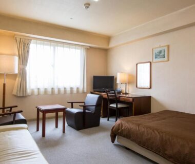 Western-style room with bed, sofa, desk and window at Komoro Grand Castle Hotel in Nagano