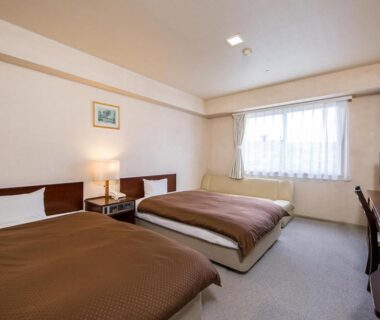 Two single beds with brown covers, bedside lamp, desk and TV at Komoro Grand Castle Hotel in Nagano