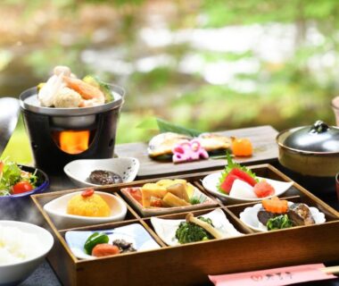 Lacquered multi-compartment tray of assorted Japanese side dishes with rice and soup on a wooden table