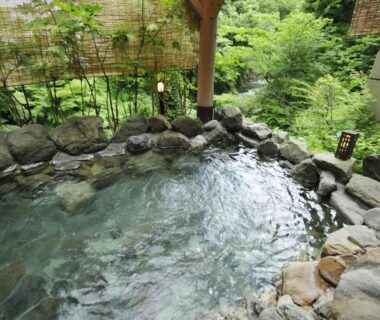 Rock-lined outdoor onsen with bamboo screen and verdant garden at Koorogirou in Ishikawa, Chūbu