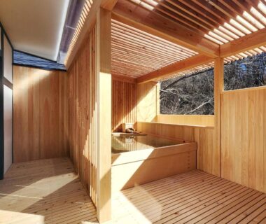 Partially enclosed wooden onsen bath with slatted roof and tub overlooking wooded hillside at Kose Onsen, Nagano