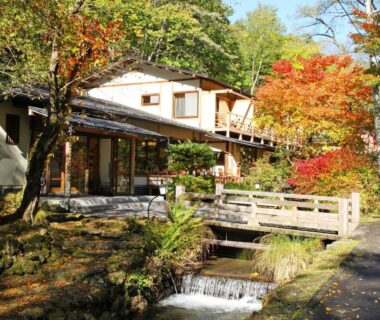 Wooden footbridge over stream with autumn foliage at Kose Onsen in Nagano